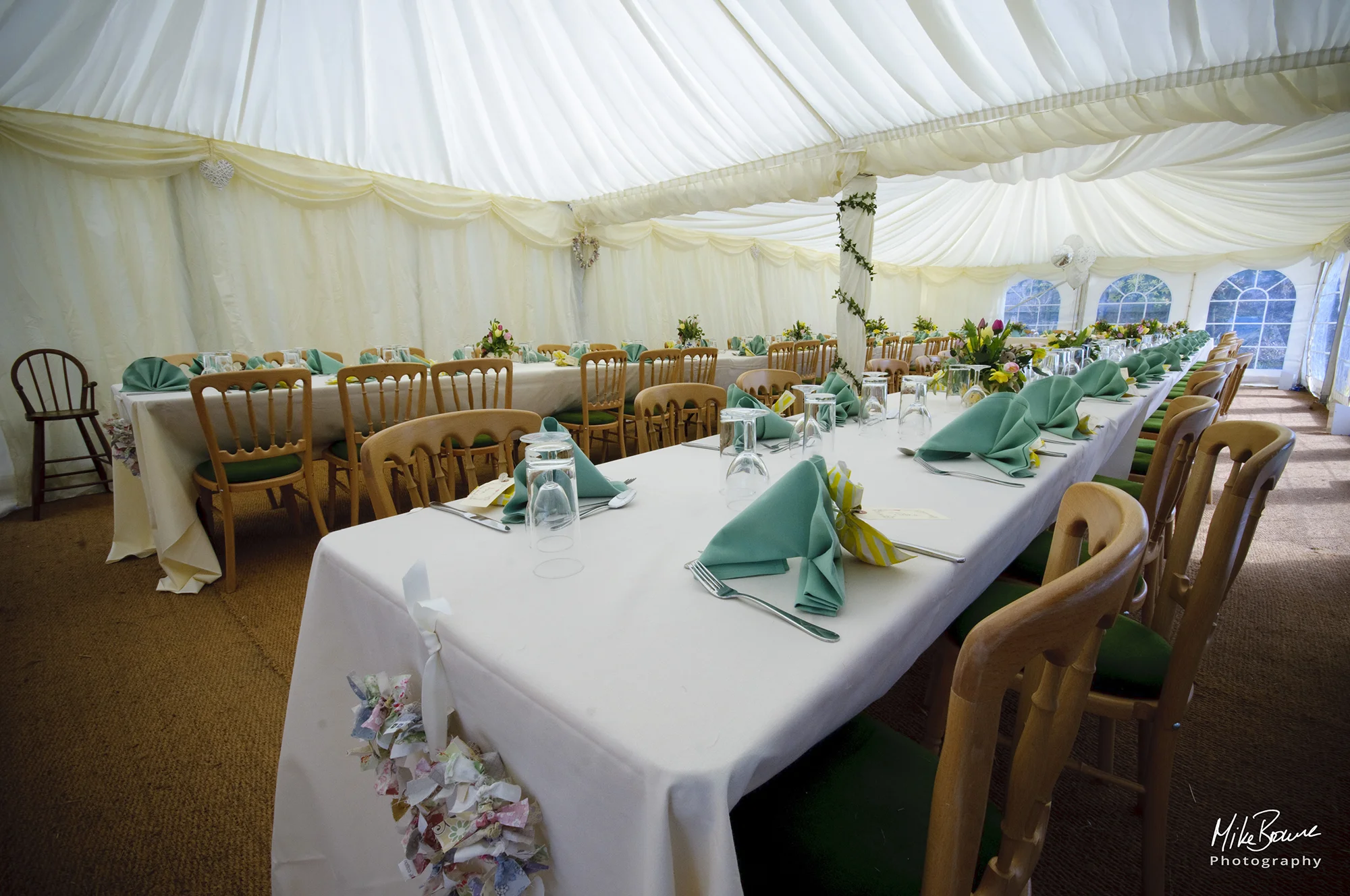 Dining tables, chairs and place settings laid out for a wedding in a white marquee