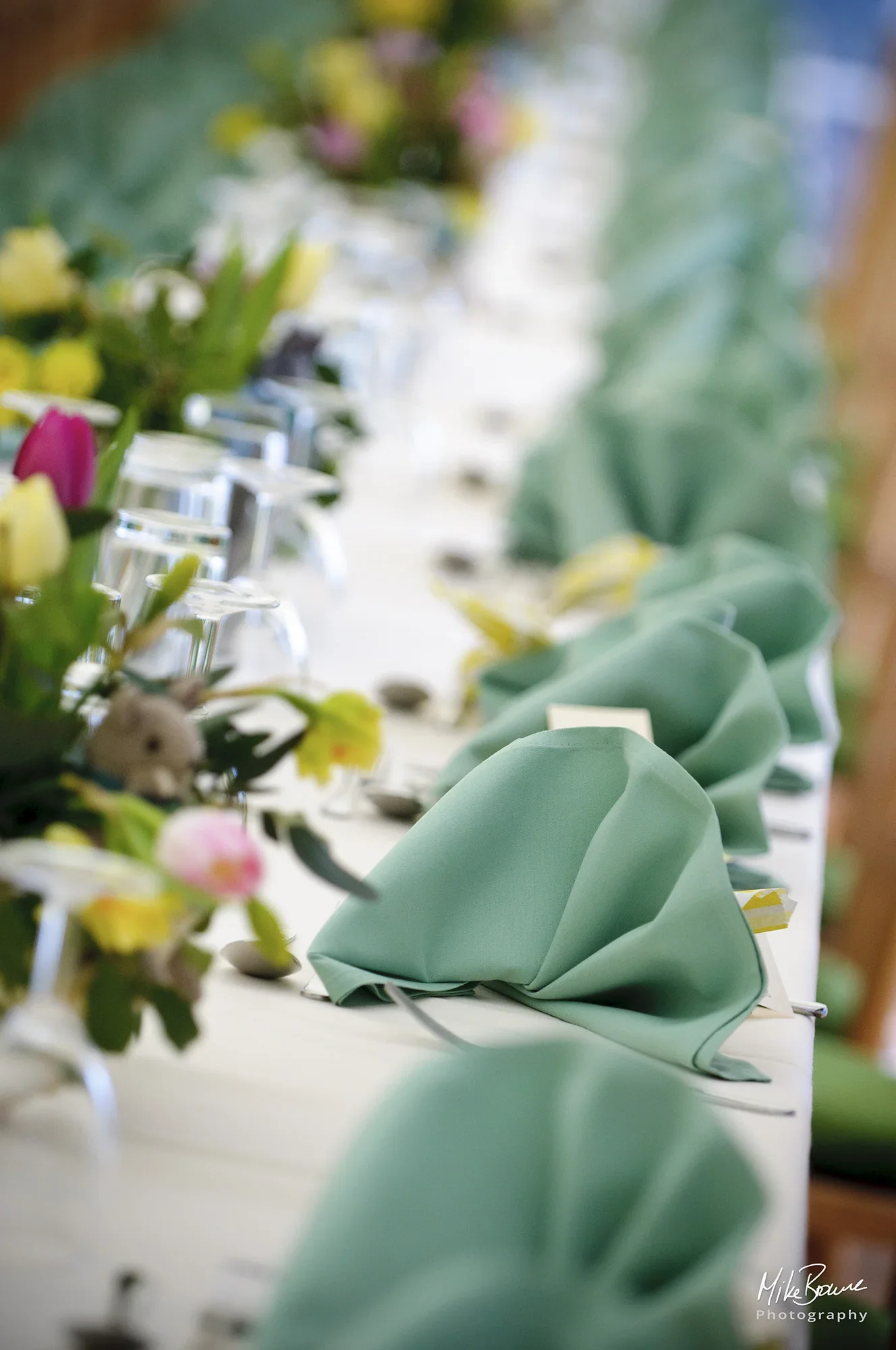 long row of green napkins, cutlery, glasses and flowers laid on a white table cloth