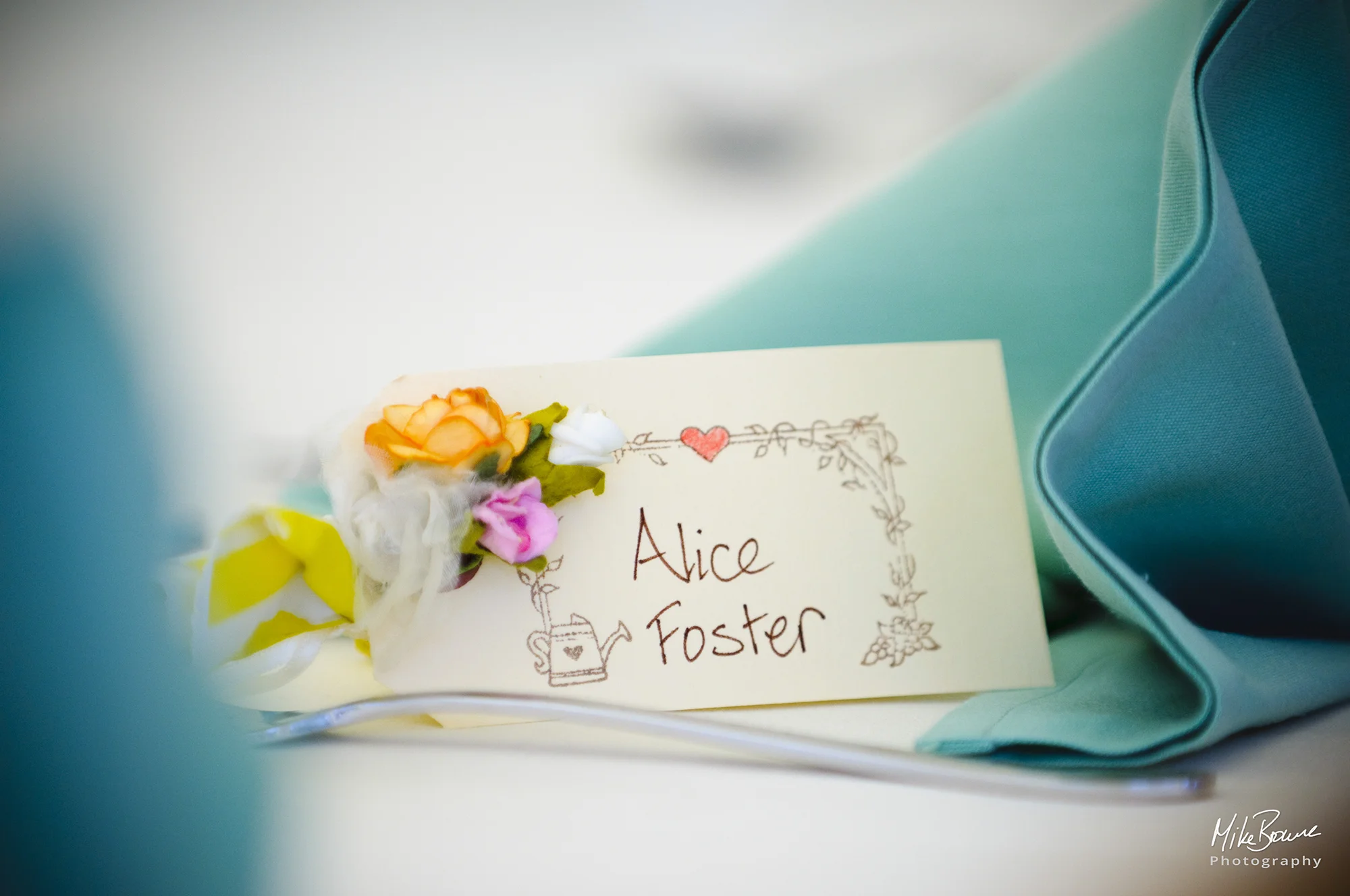 Place card with tiny bouquet of yellow pink and white flowers between two decoratively folded napkins