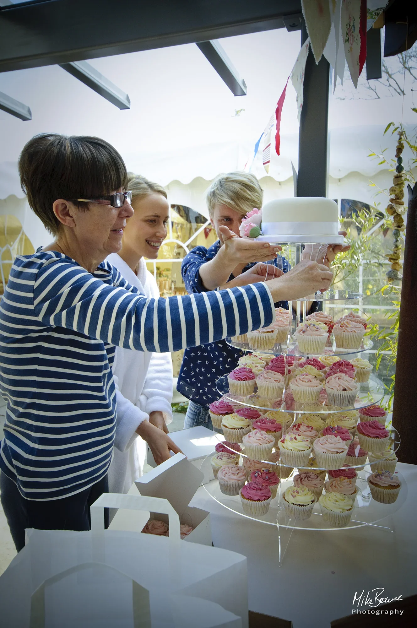 Three women placing top tier of a wedding cake on a display stand