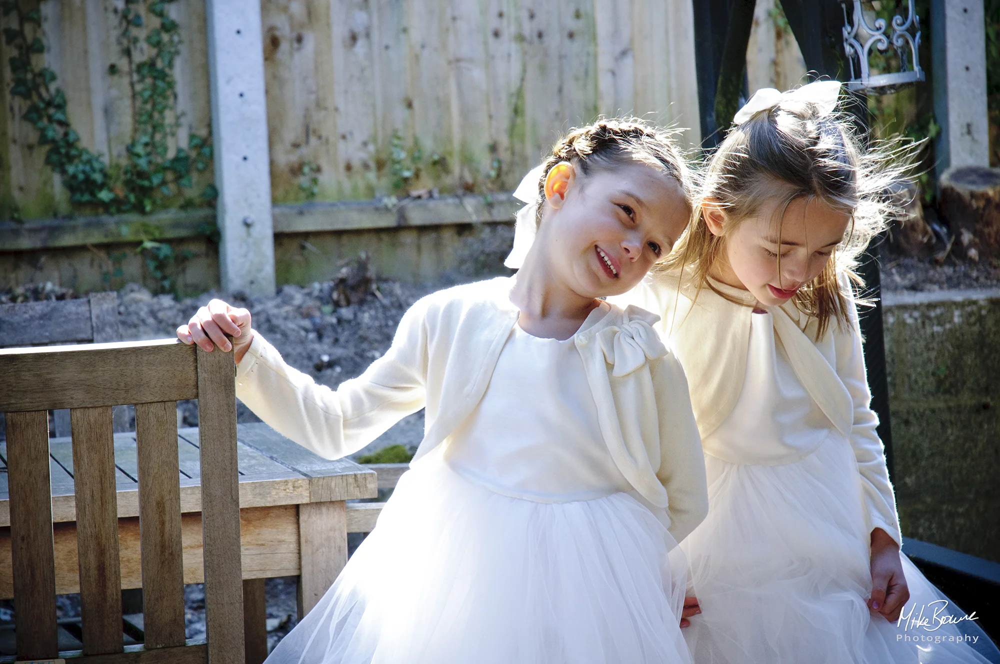 Two small girls dressed as flower girls laughing in sunshine