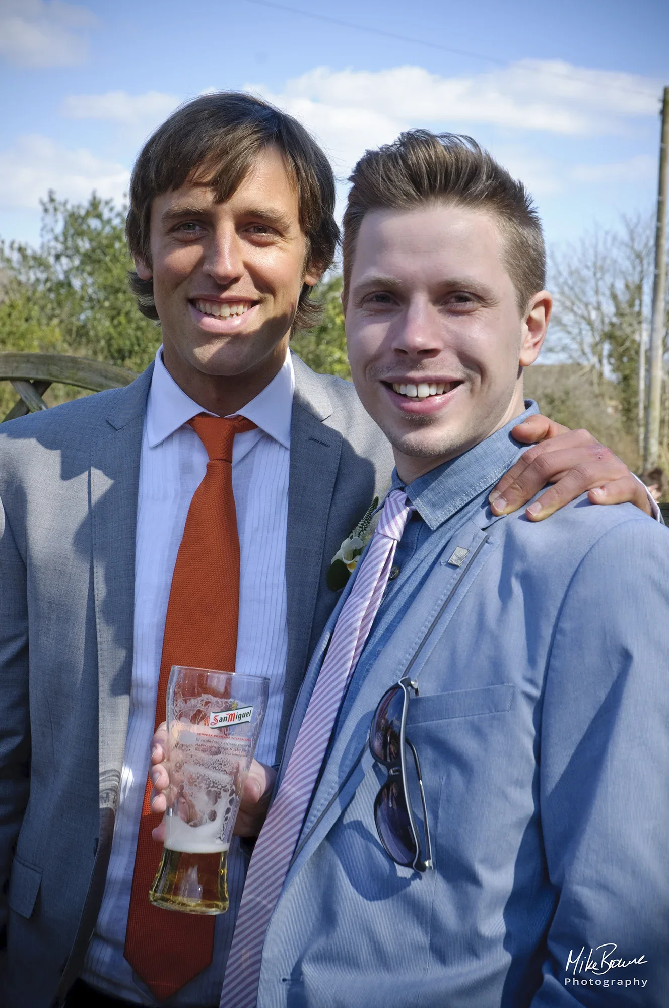 Man with his arm round shoulders of another man who is holding a glass of beer