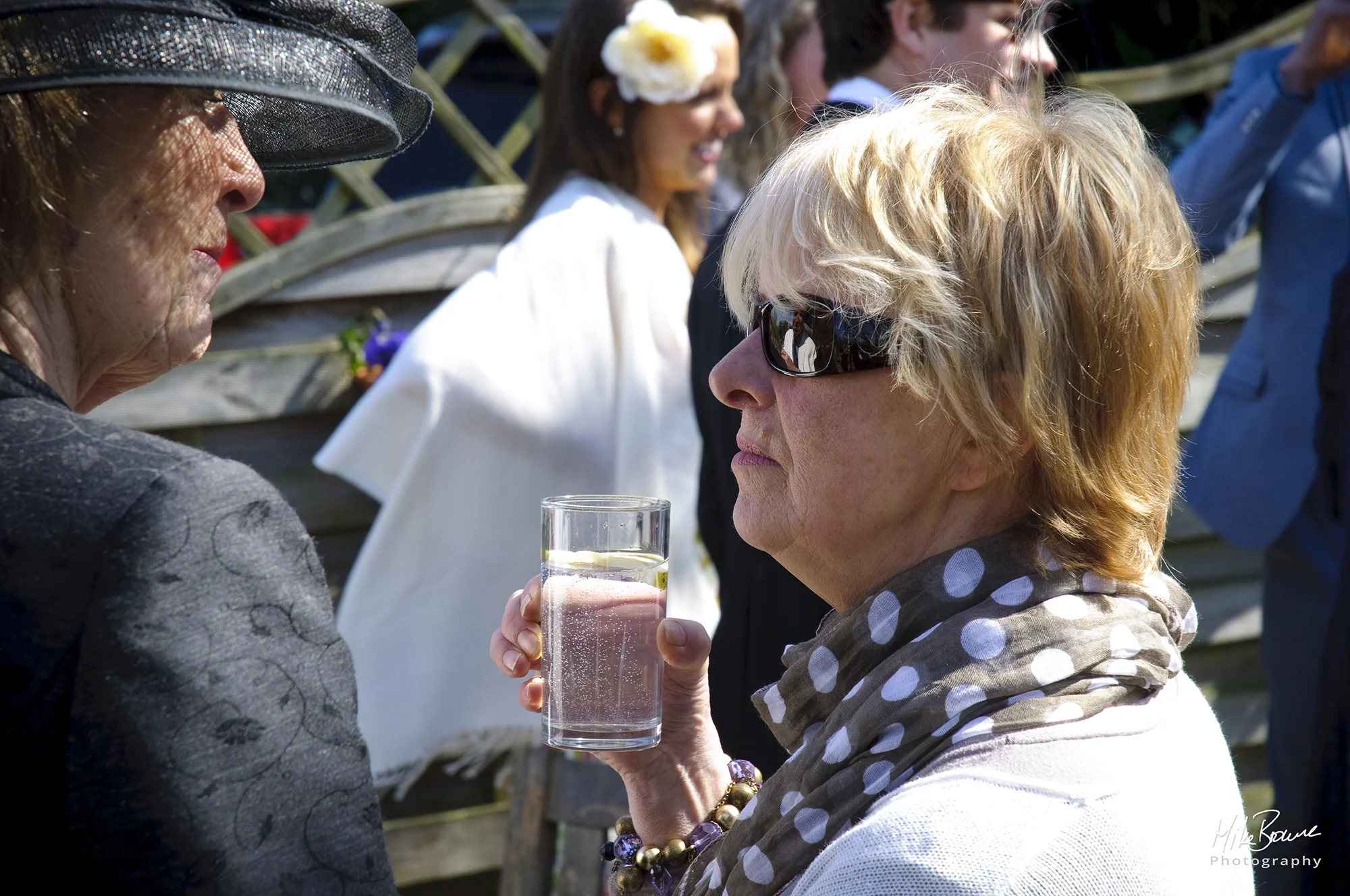 Lady in dark hat talking to a lady wearing sunglasses at pre wedding drinks