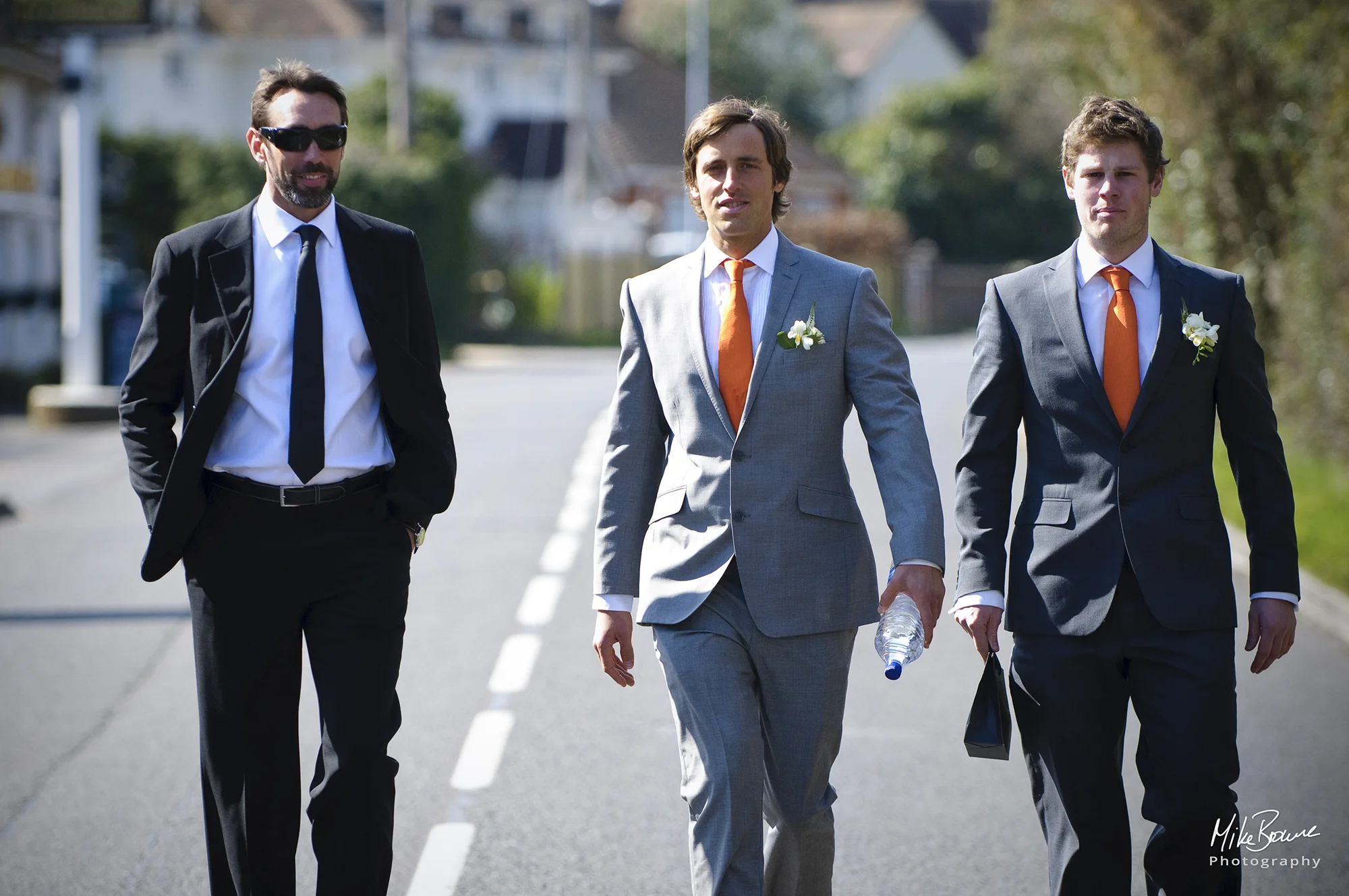 Groom and his best men striding along centre of road on way to the church