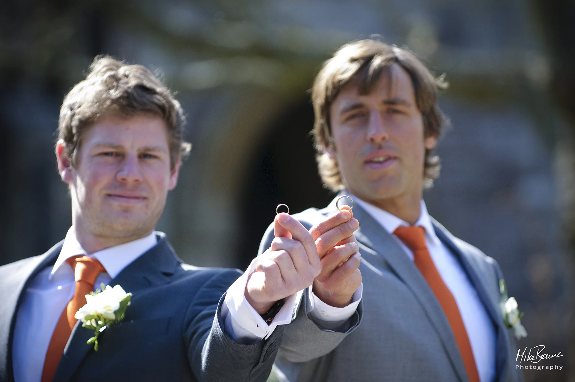 Groom and best man holding the wedding rings at arm\'s length towards the camera