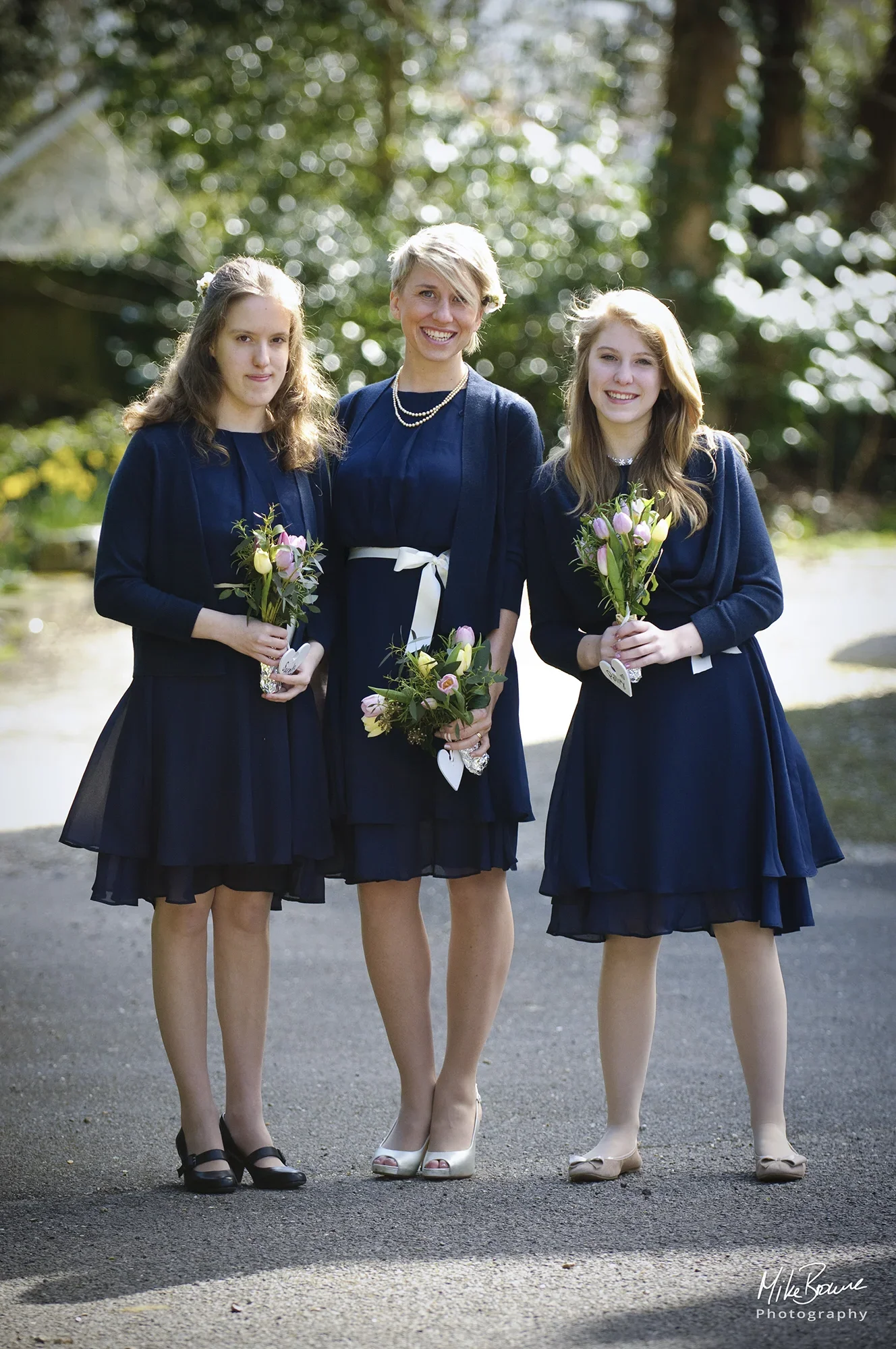 Three bridesmaids in blue dresses holding bouquets of flowers