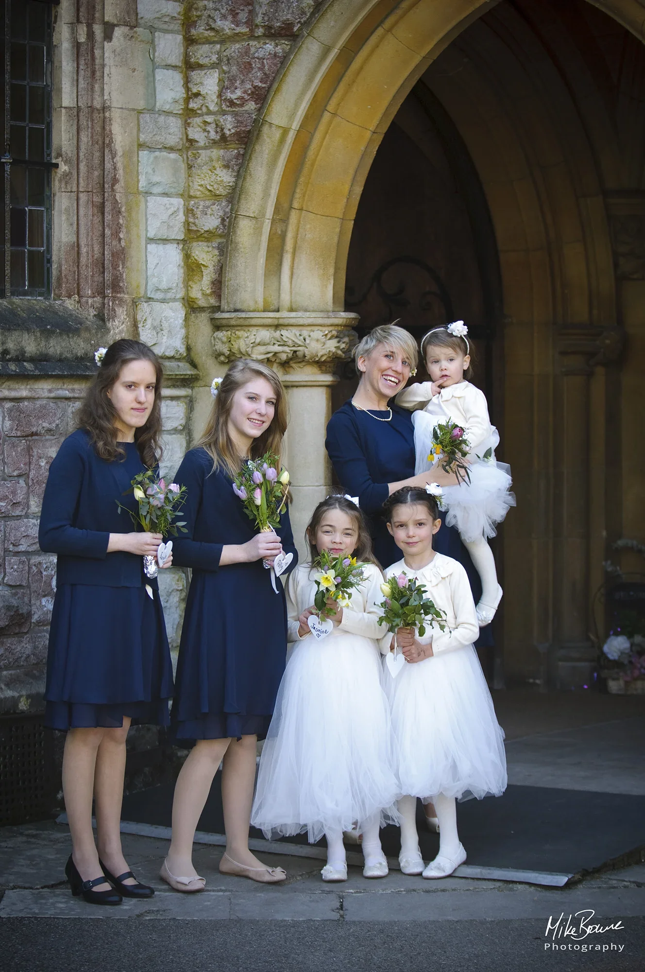 Bridesmaids i blue dresses with small flower girls in white dresses in the church doorway