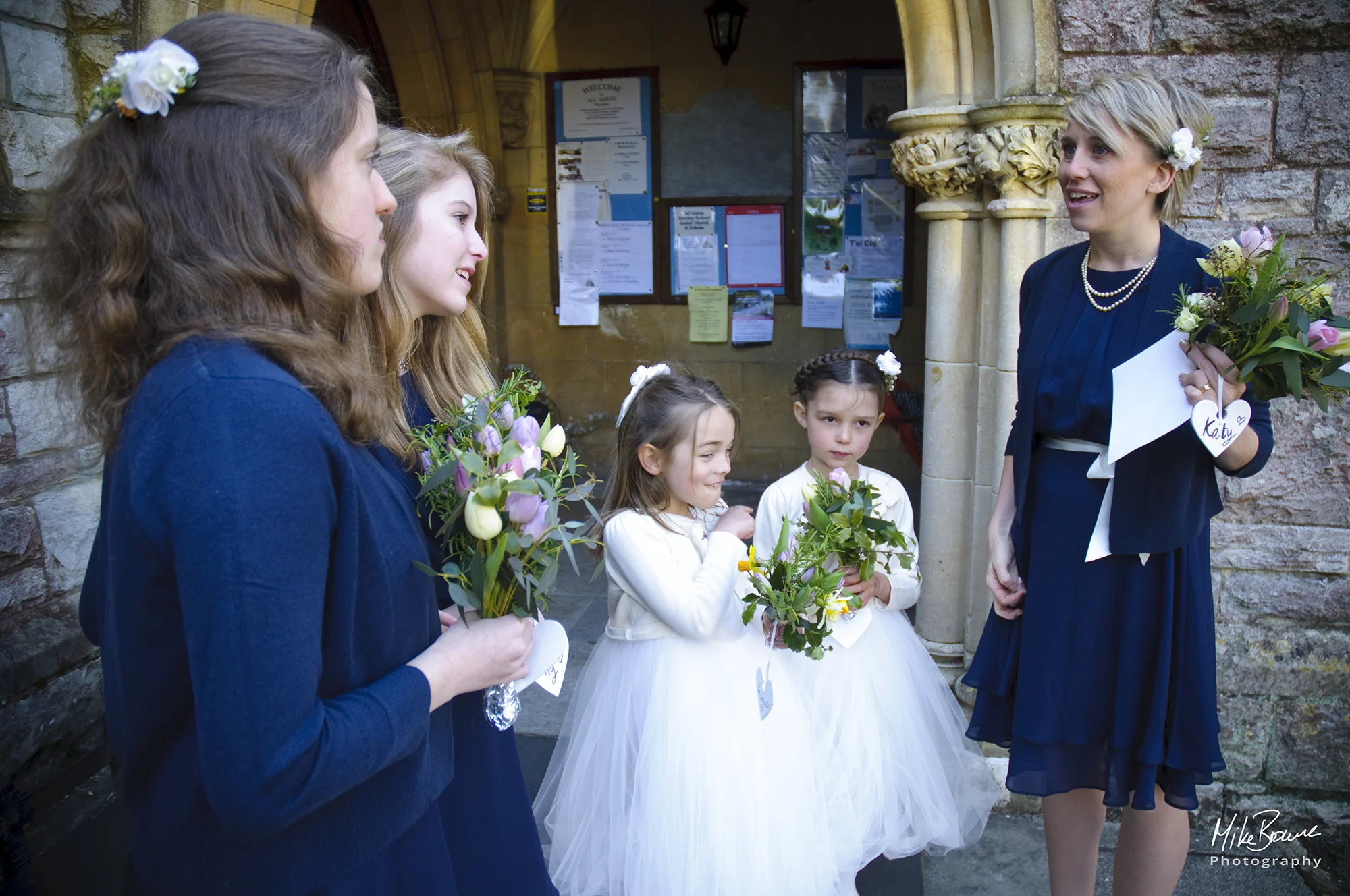 Bridesmaids and flower girls in conversation in a church doorway