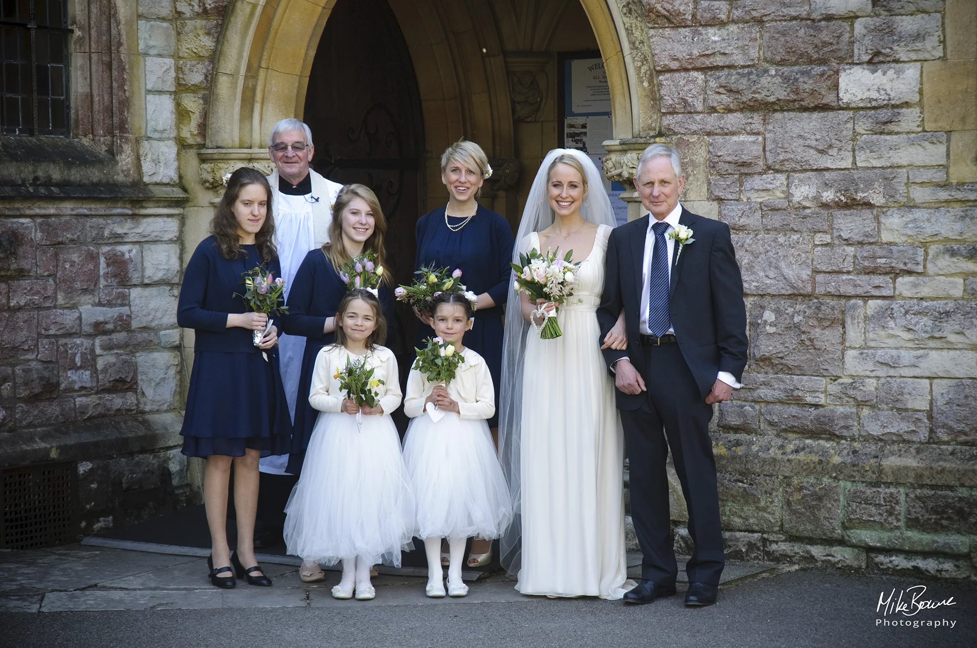 The bride with her father, bridal party and vicar in the church doorway