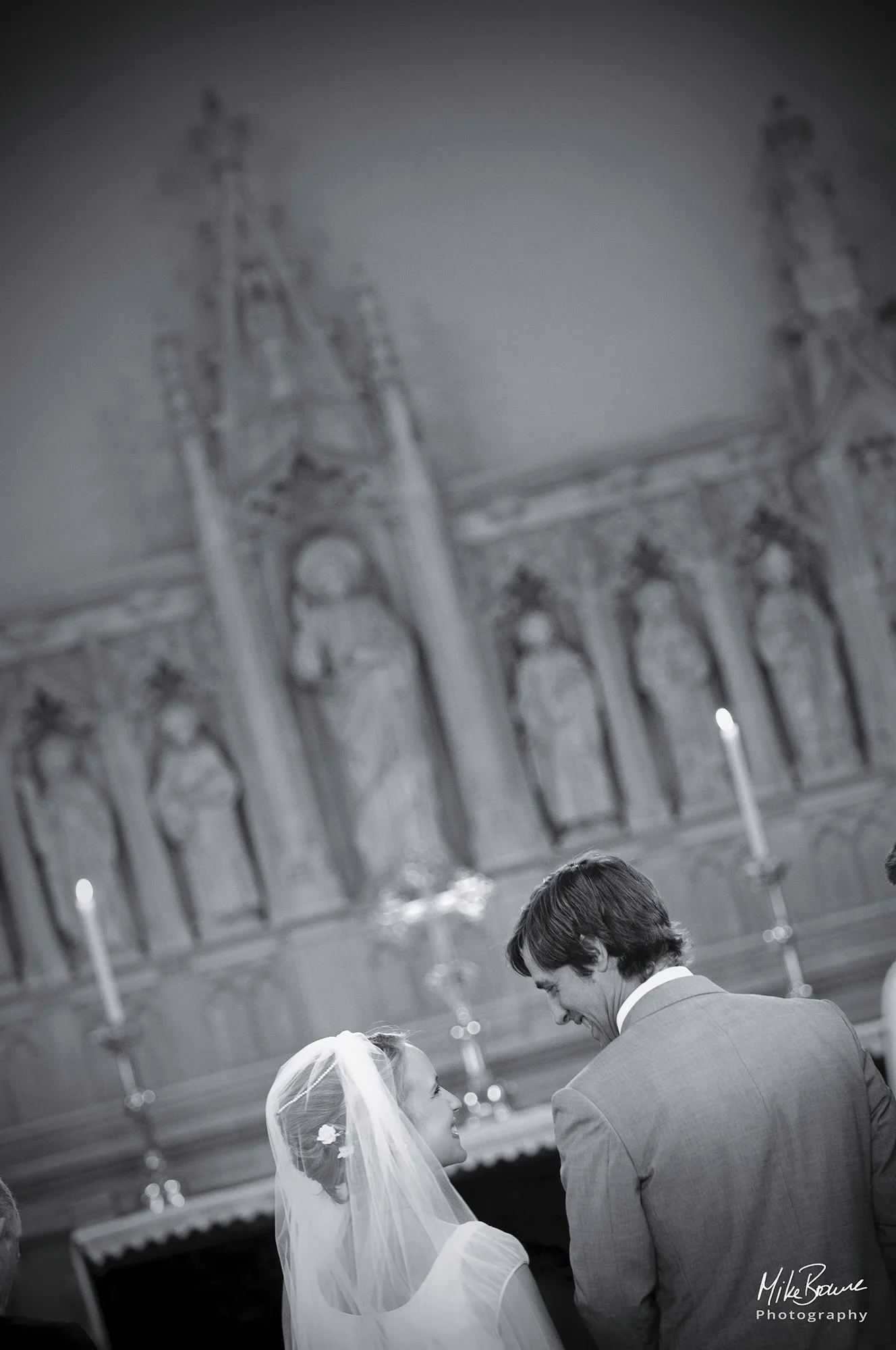 wedding couple turn and laugh together with church alter and candles beyond