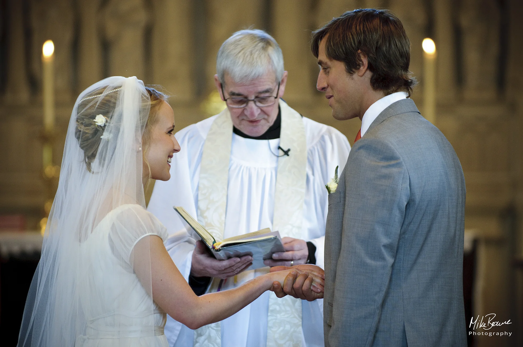 Man holding his brides hand as vicar reads from the bible