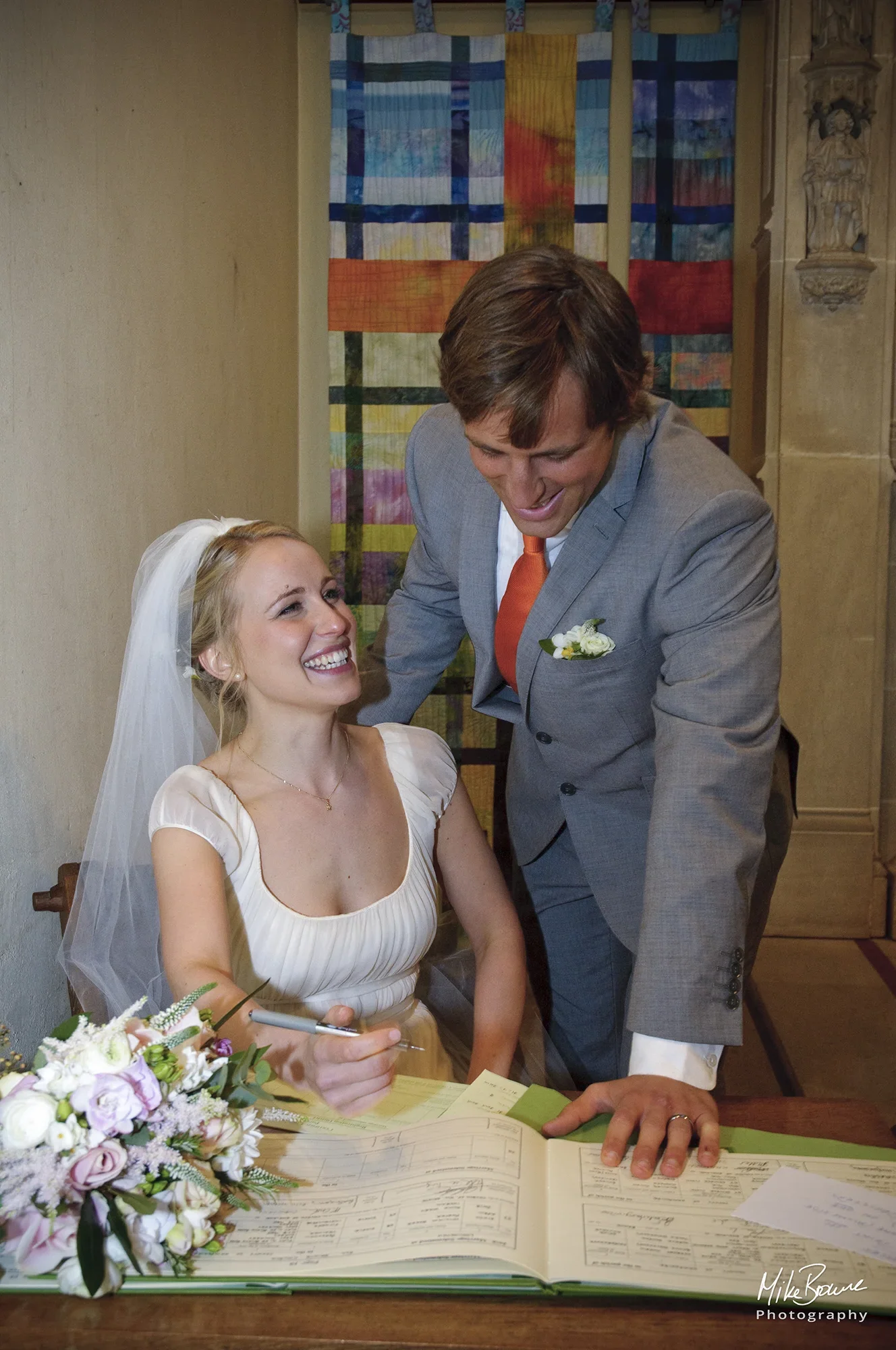 newly married couple looking at each other whilst signing the register